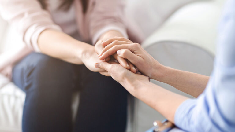 Two people sitting together, one gently holding the other's hands in support