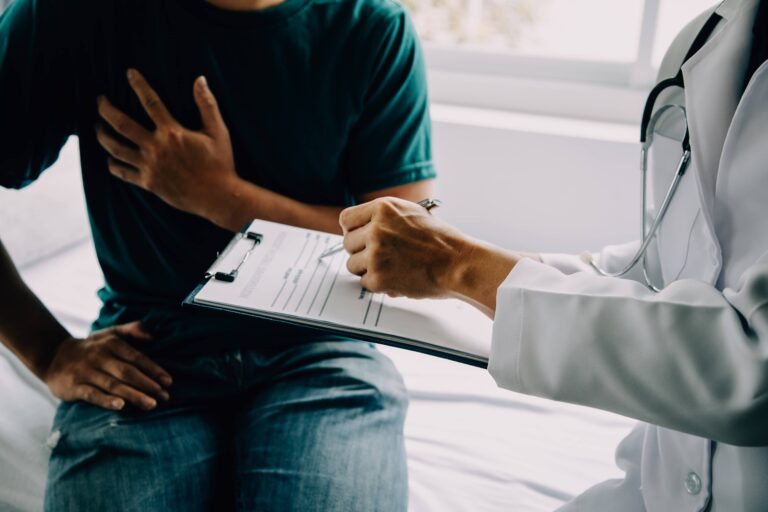 A patient holding their chest while a doctor takes notes on a clipboard
