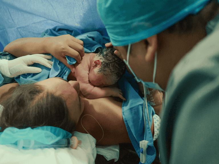 A mother holding her newborn baby skin to skin moments after birth, with a clinician beside them